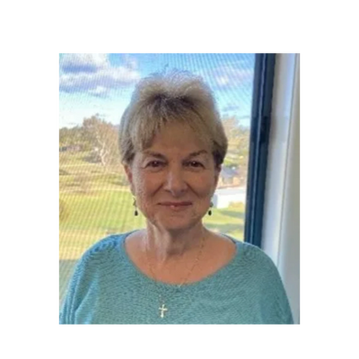 Smiling woman in a light blue sweater by a window.