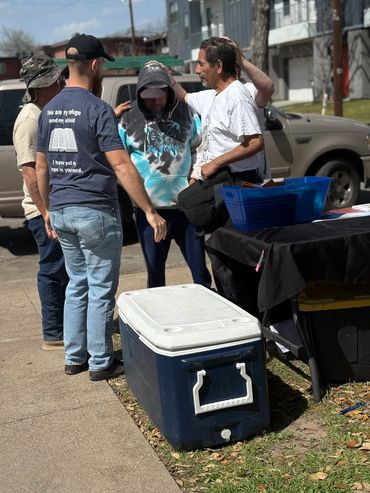 Four people conversing near a cooler and table outdoors on a sunny day.