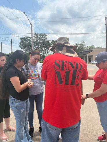 Group praying outdoors with person wearing a red 'SEND ME' shirt.