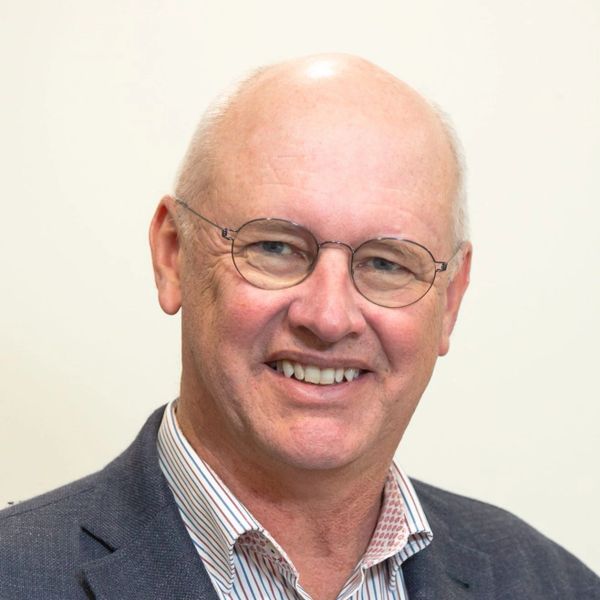 Smiling older man with glasses in a blazer and striped shirt.