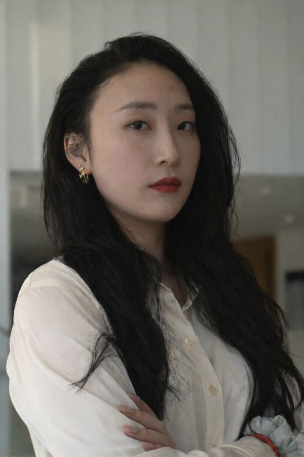 Confident woman with long black hair and gold earrings in a white shirt.