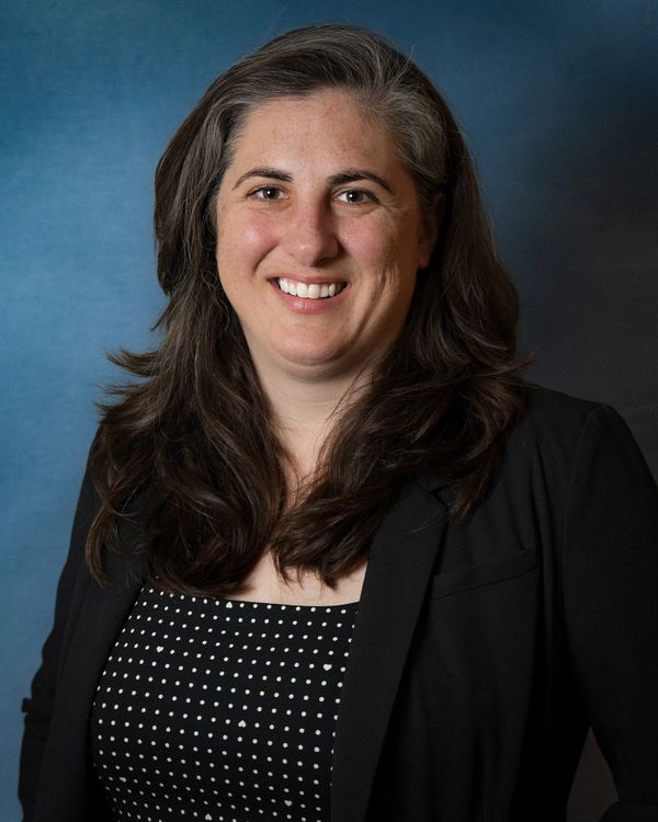 Professional woman smiling, wearing a black blazer and polka dot top.