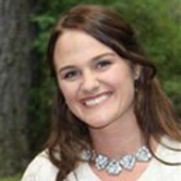 Smiling woman with brown hair and a statement necklace outdoors.