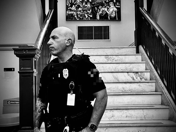 Black and white photo of a security guard standing near a marble staircase indoors.