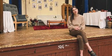 Young woman sitting thoughtfully on an old wooden stage in a cozy room.