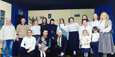 Group photo of adults and children dressed formally in an indoor setting.