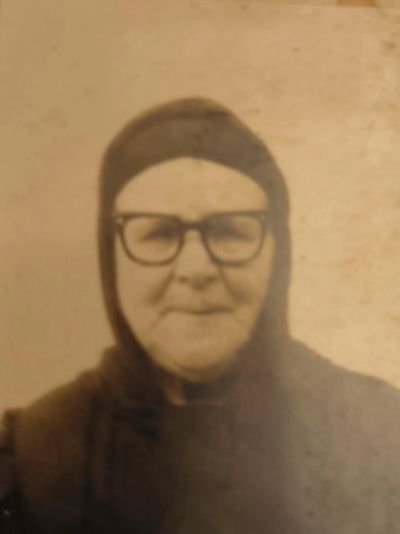 Portrait of an elderly woman wearing glasses and a headscarf in a vintage photo.