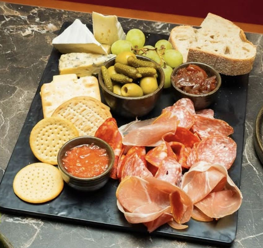 A charcuterie board with meats, cheeses, crackers, grapes, and condiments.