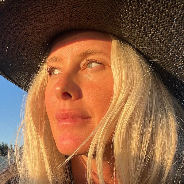 Woman with long blonde hair wearing a large black hat in golden sunlight.