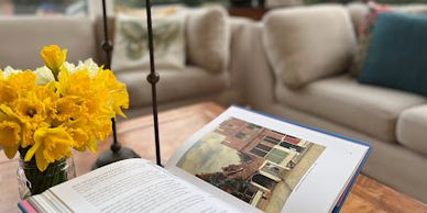 wood coffee table with an open art album, bright yellow daffodils and bronze vintage candle holders