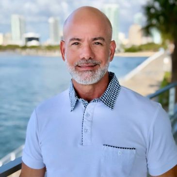 Smiling bald man with a beard by the water.