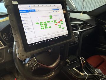 Diagnostic tablet mounted on BMW steering wheel displaying system topology.
