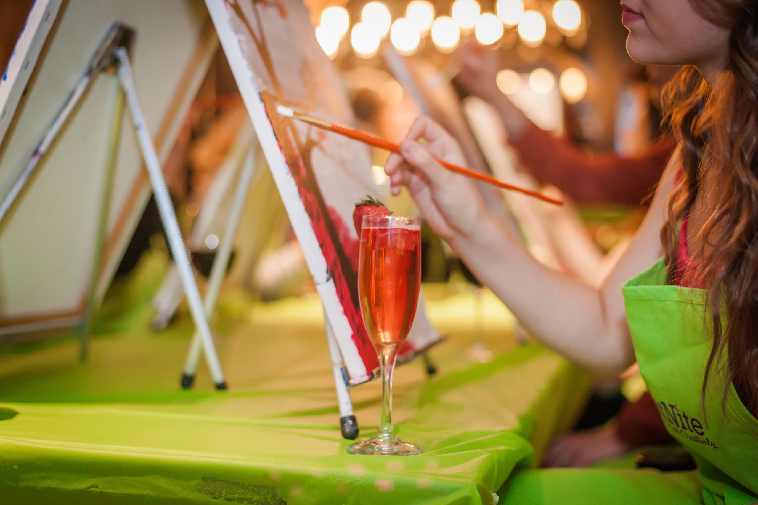 Person painting on canvas with a cocktail on the table.