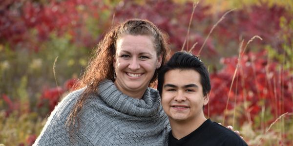 Woman with curly hair wearing a gray sweater with a boy with black hair wearing a black shirt standi