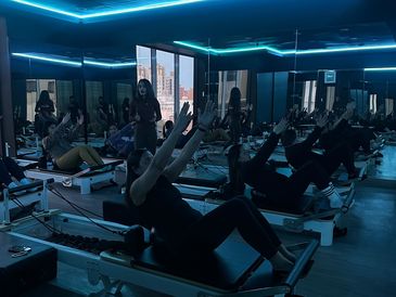 People exercising on reformer machines in a mirrored Pilates studio.