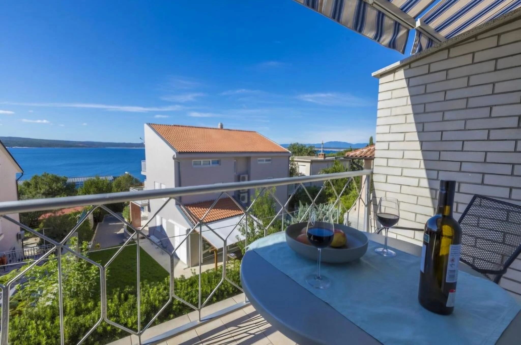 Balcony with a sea view, wine, and fruit bowl.
