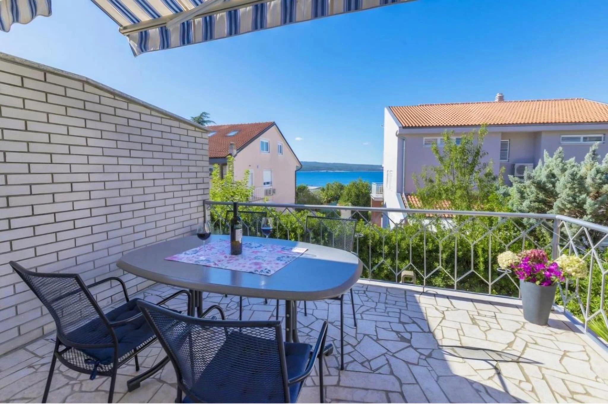 Sunny balcony with table, chairs, and sea view.