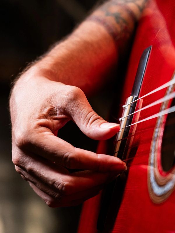 Close-up of a hand plucking strings on a red acoustic guitar.