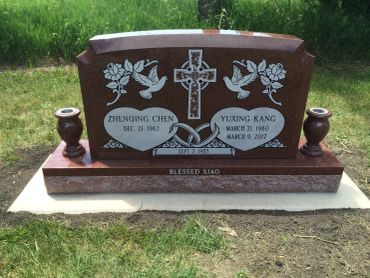 Double heart tombstone with cross and doves in a grassy cemetery.