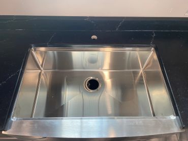 Shiny stainless steel kitchen sink installed in black countertop.
