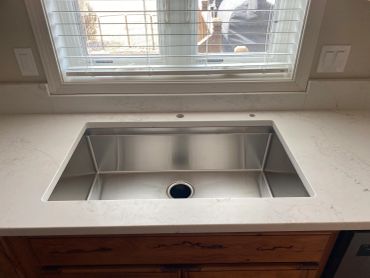 Shiny stainless steel kitchen sink under a window.