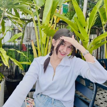 Young woman smiling outdoors with greenery behind her.