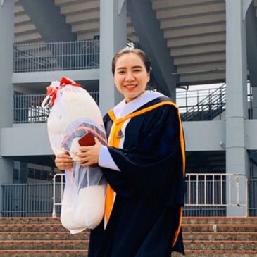 Happy graduate holding a large stuffed toy in front of stairs.