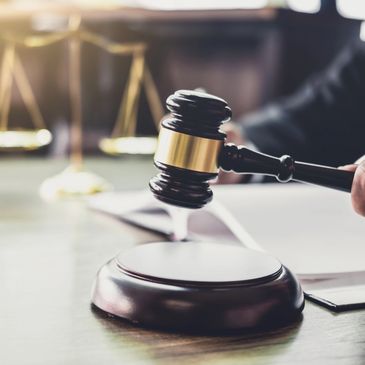 Judge striking gavel in courtroom with scales of justice in background.