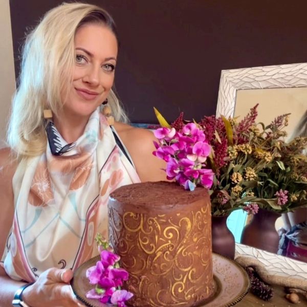 Woman holding a beautifully decorated chocolate cake with purple flowers.