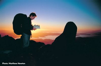 Man wearing a large pack reading a map against a sunrise