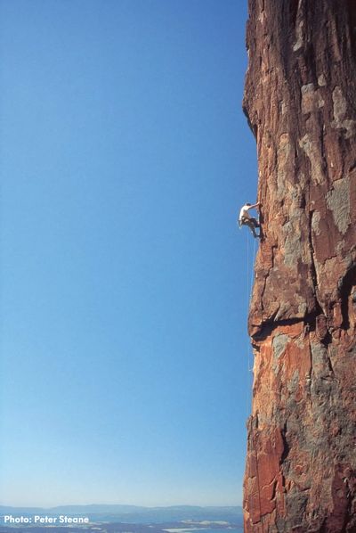 a lone rock climber three quarters of the way up an exposed rock face