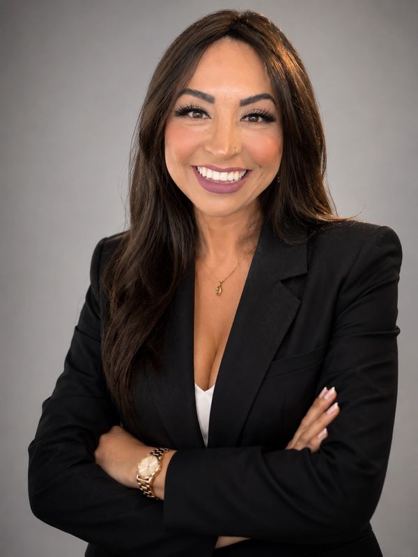 Confident woman in a black blazer smiling with arms crossed.