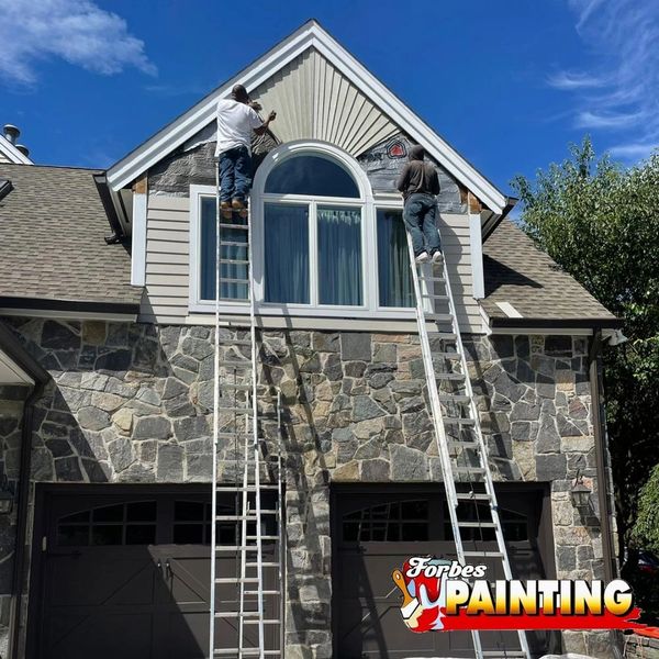 Two painters working on a house exterior under a clear blue sky.