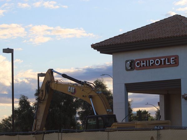 Construction equipment near a Chipotle restaurant during sunset.