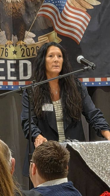 Woman speaking at a podium with patriotic backdrop.