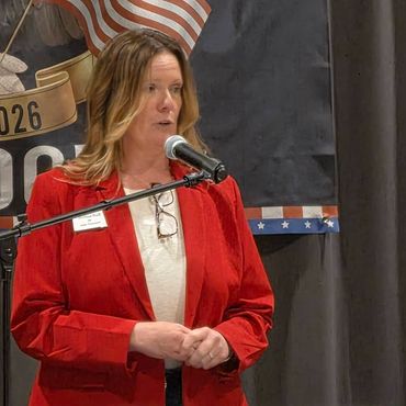 Woman in red jacket speaking at a microphone indoors.