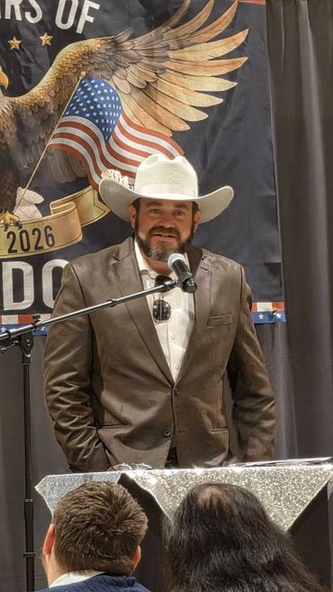 Man in cowboy hat speaking at a podium with an American flag backdrop.