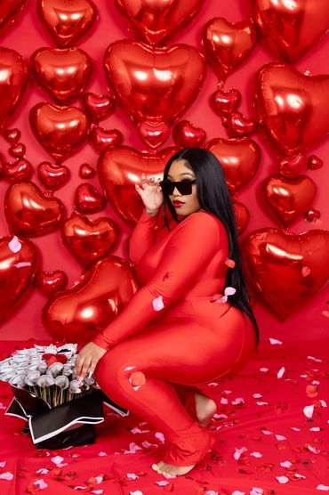 Woman in red outfit with heart balloons and rose petals.