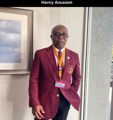 A man in a maroon blazer with a name tag stands indoors.