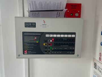 Fire alarm control panel and manual with a red alarm button below.