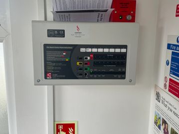 Fire alarm control panel and manual with a red alarm button below.