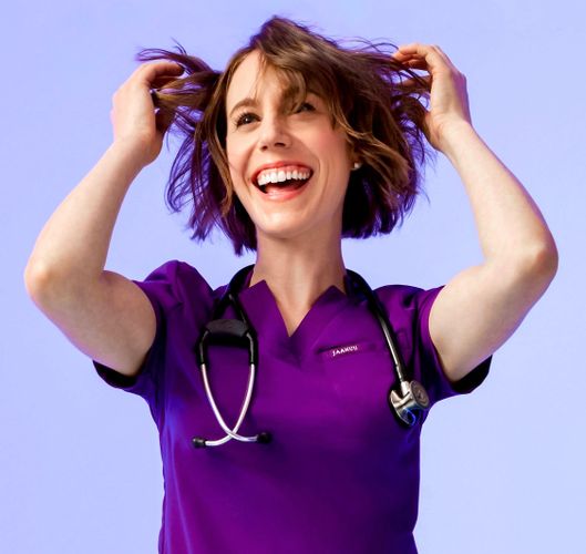 Smiling healthcare professional in purple scrubs playing with her hair.