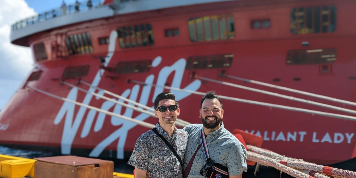 Two men in front of cruise ship Virgin Voyages Valiant Lady