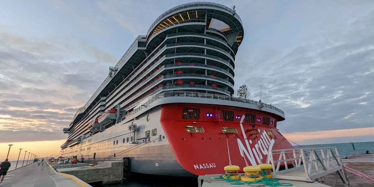 Luxury Virgin Voyages cruise ship at sea with a sunset background.