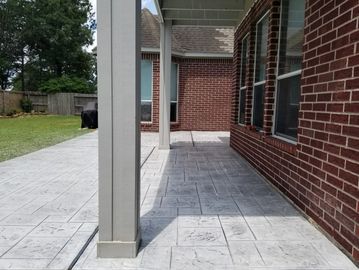Concrete patio with stamped pattern next to a brick house.