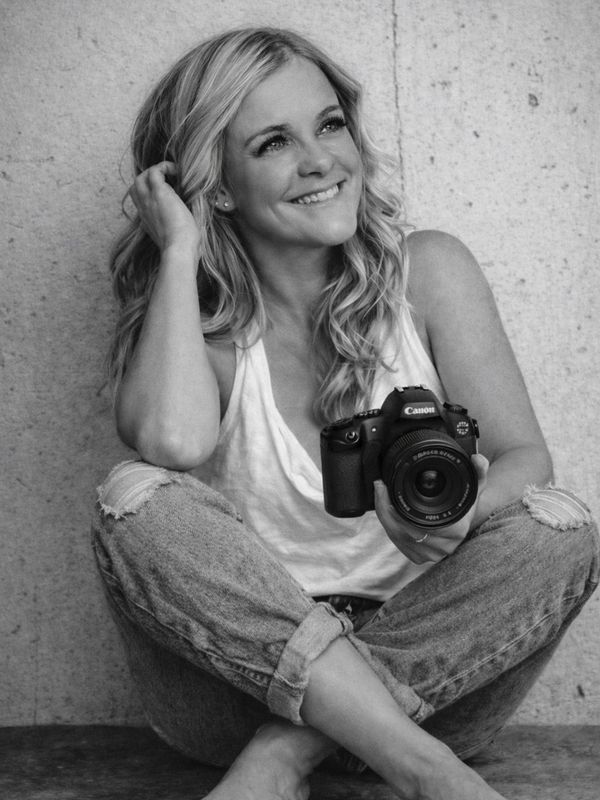 Smiling woman sitting cross-legged holding a Canon camera.