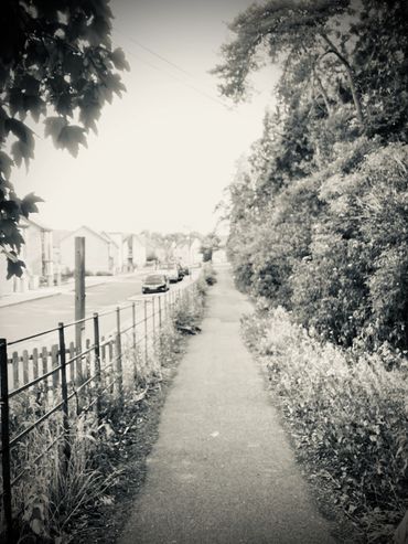 A pathway stretching into a soft focus horizon with a modern street to one side in black and white.