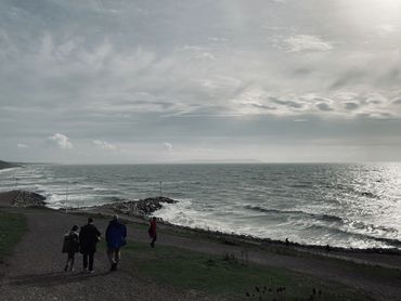 A choppy sea on an overcast day with a grey, rocky hillside and a few people in the foreground.