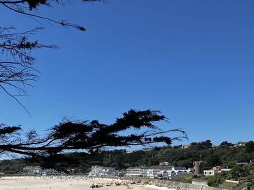 A large, blue cloudless sky with a sandy bay in the foreground, adorned by buildings in the distance