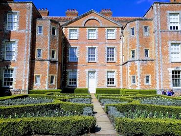 A large, redbrick stately home and front garden in bright, vibrant colours.